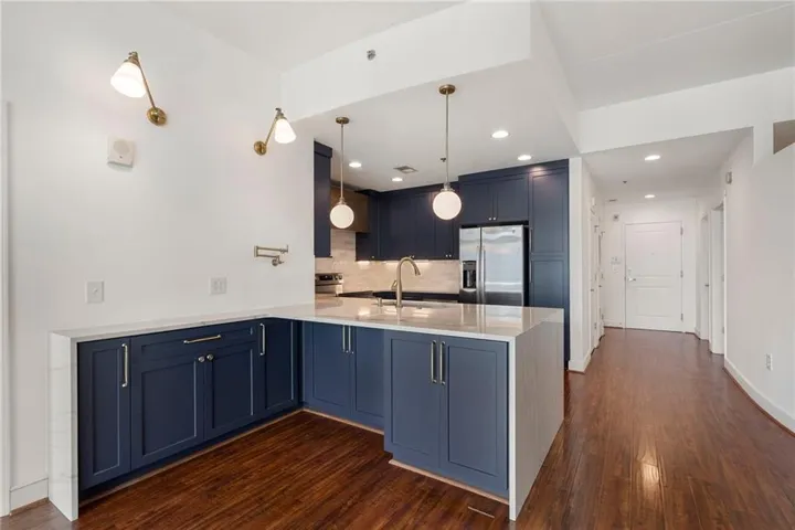 Modern kitchen featuring navy cabinetry, white countertops, stainless steel appliances, and a marble-finish backsplash