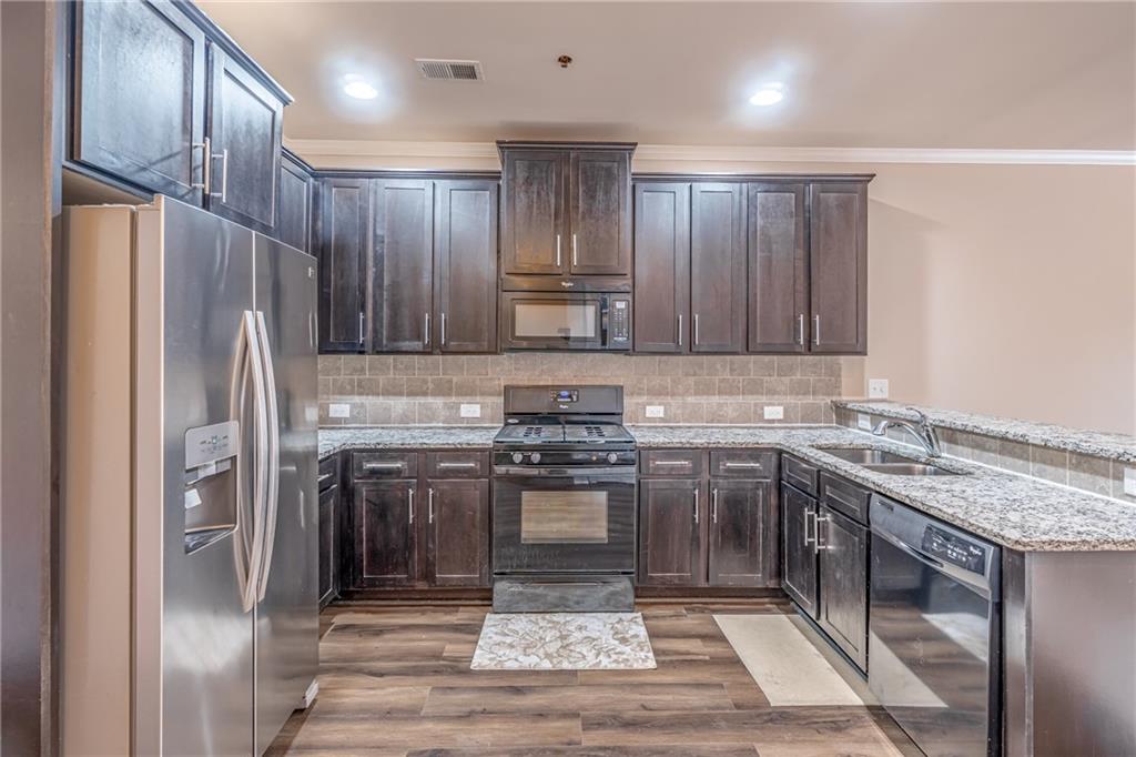 Kitchen featuring light hardwood / wood-style flooring, black appliances, dark brown cabinets, and light stone countertops Kitchen featuring light hardwood / wood-style flooring, black appliances, dark brown cabinets, and light stone countertops