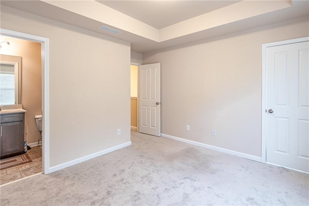 Unfurnished bedroom with connected bathroom, a raised ceiling, and light carpet Unfurnished bedroom with connected bathroom, a raised ceiling, and light carpet