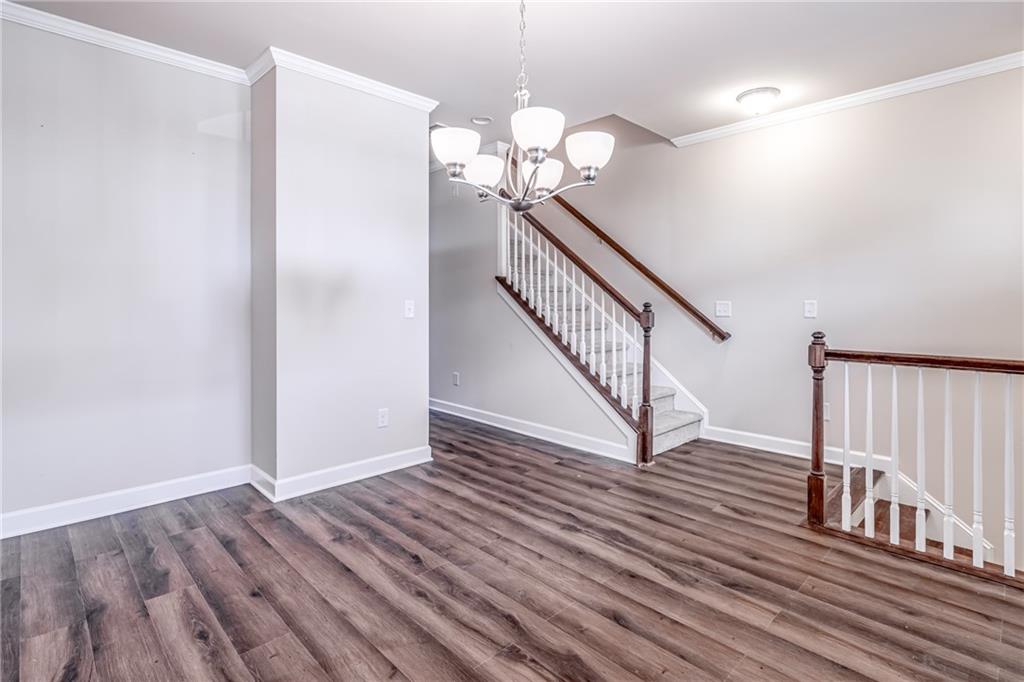 Unfurnished room with crown molding, dark hardwood / wood-style flooring, and a notable chandelier Unfurnished room with crown molding, dark hardwood / wood-style flooring, and a notable chandelier
