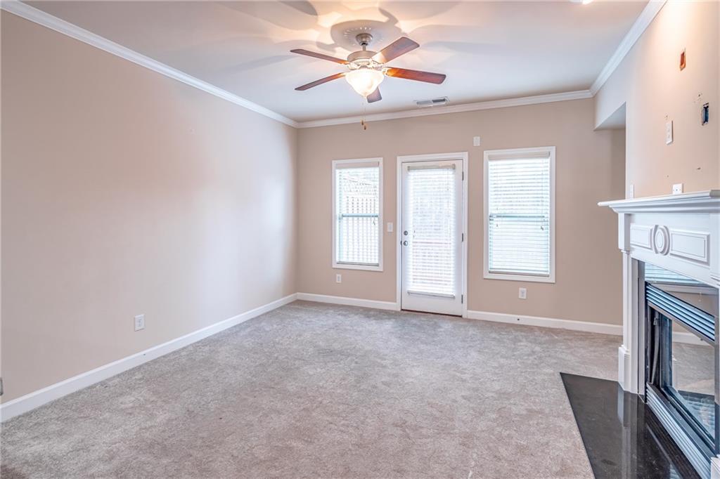 Unfurnished living room with ceiling fan, light colored carpet, and ornamental molding Unfurnished living room with ceiling fan, light colored carpet, and ornamental molding