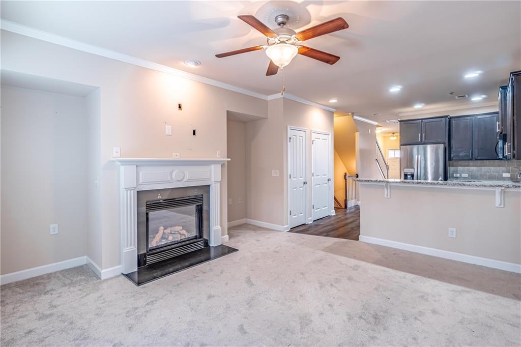 Unfurnished living room featuring ornamental molding, light colored carpet, and ceiling fan Unfurnished living room featuring ornamental molding, light colored carpet, and ceiling fan