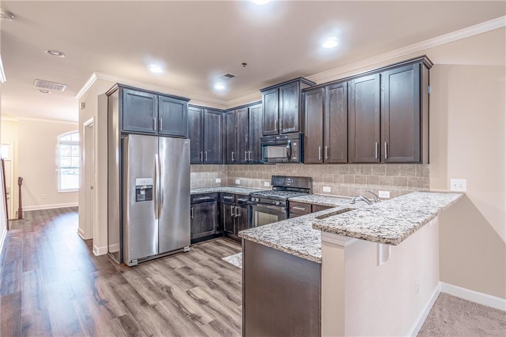 Kitchen featuring light stone counters, stainless steel fridge, light wood-type flooring, gas stove, and tasteful backsplash Kitchen featuring light stone counters, stainless steel fridge, light wood-type flooring, gas stove, and tasteful backsplash