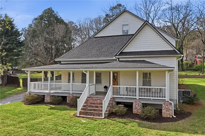 Expansive wrap-around porch with white railings, brick foundation, and dark shingle roof
