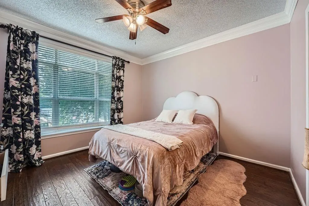 Bedroom with a textured ceiling, multiple windows, wood finished floors, crown molding, and ceiling fan