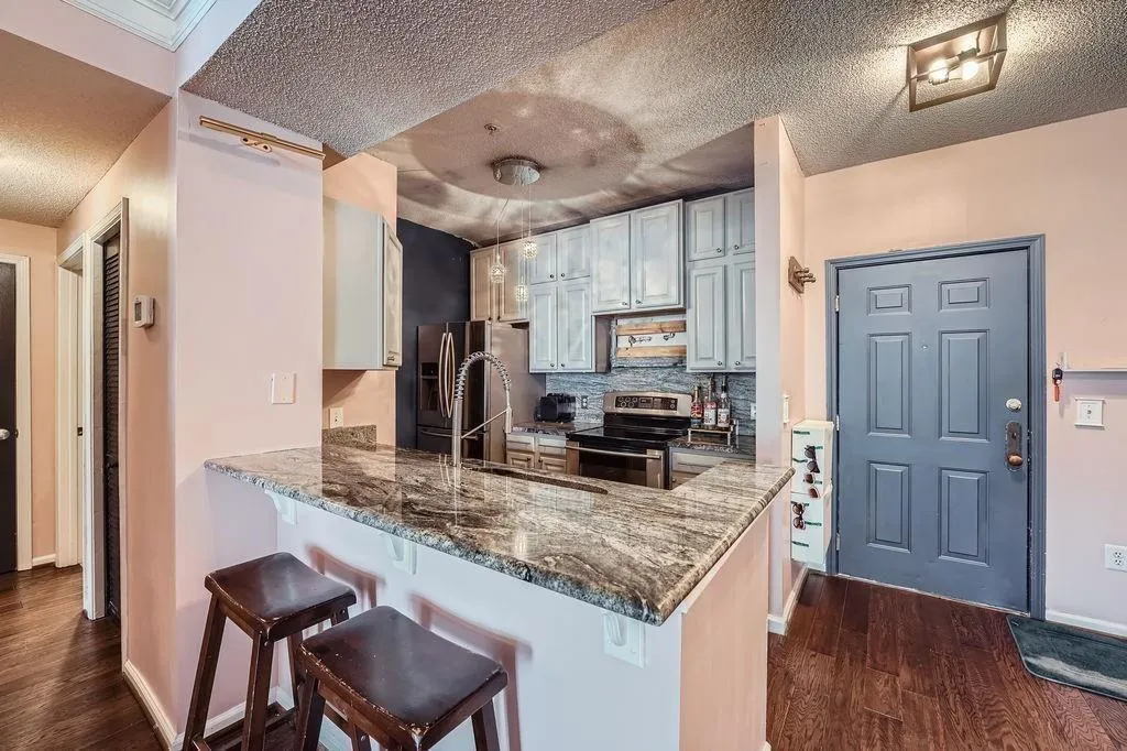 Kitchen with stainless steel appliances, a peninsula, dark wood finished floors, a kitchen bar, and decorative backsplash