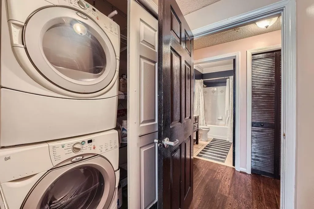 Laundry room featuring stacked washer / drying machine, dark wood-style flooring, and a textured ceiling