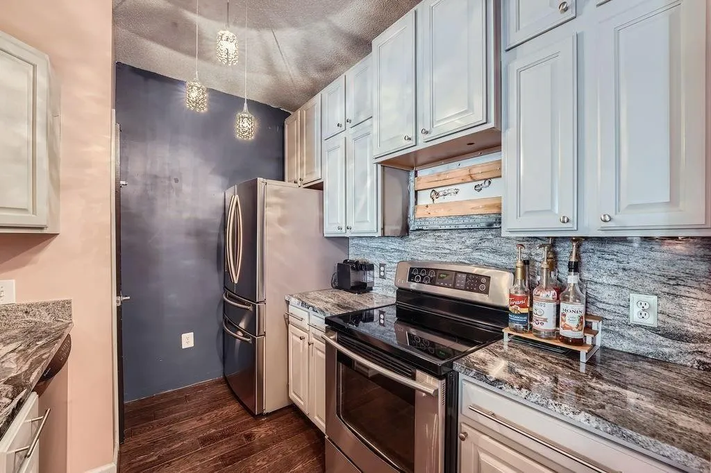 Kitchen featuring appliances with stainless steel finishes, dark wood-style flooring, decorative backsplash, pendant lighting, and dark stone countertops