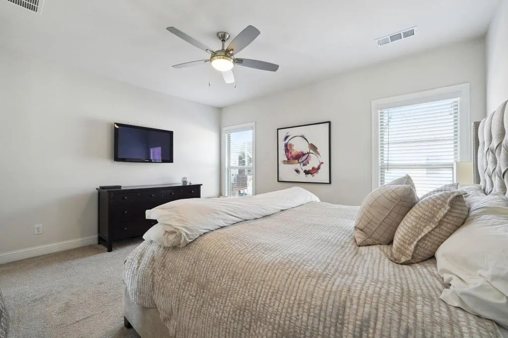 Carpeted bedroom with ceiling fan and multiple windows
