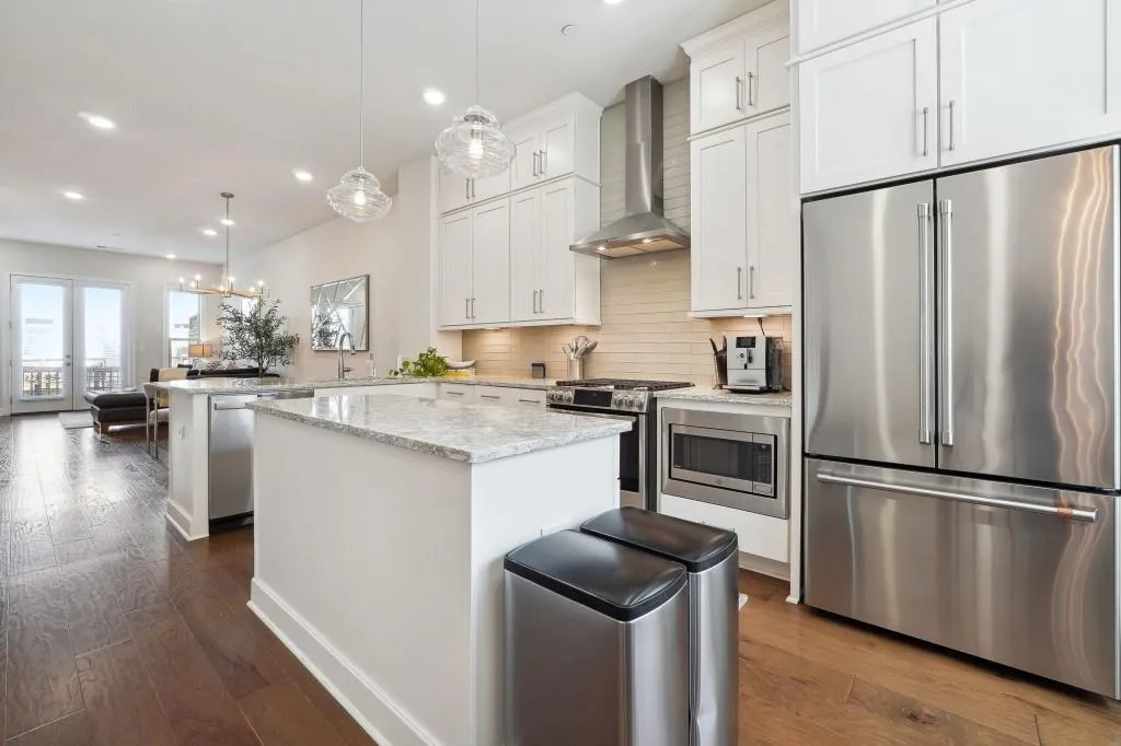 Kitchen featuring built in appliances, backsplash, hanging light fixtures, wall chimney exhaust hood, and dark hardwood / wood-style flooring
