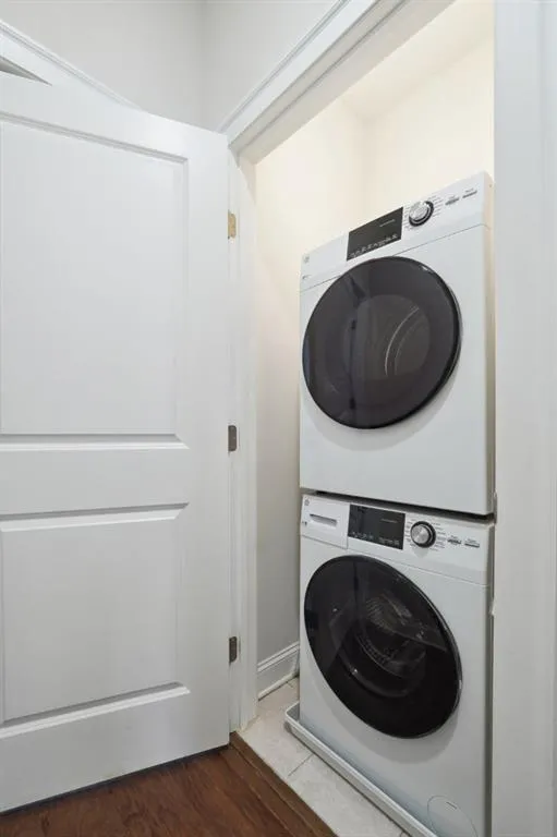 Laundry room featuring stacked washer and dryer and dark wood-type flooring