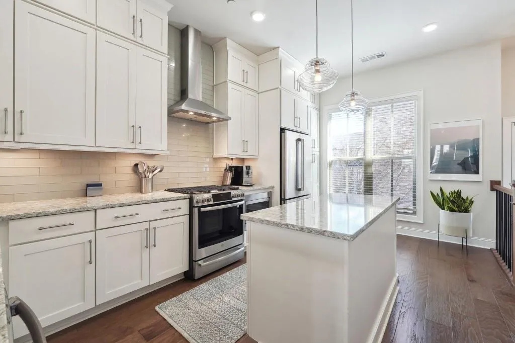Kitchen featuring appliances with stainless steel finishes, wall chimney exhaust hood, a kitchen island, backsplash, and pendant lighting