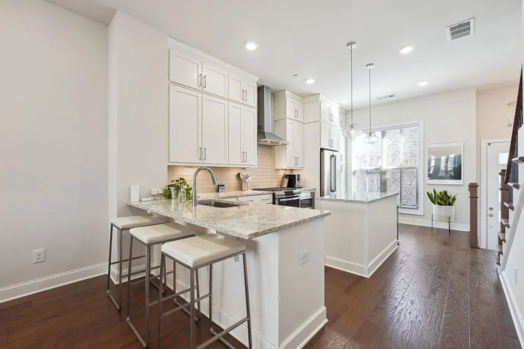 Kitchen with hanging light fixtures, stainless steel appliances, wall chimney range hood, sink, and dark hardwood / wood-style flooring