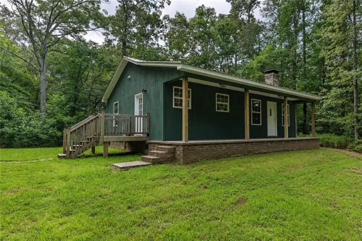 Green horizontal siding exterior with a covered front porch featuring wood posts and a brick base