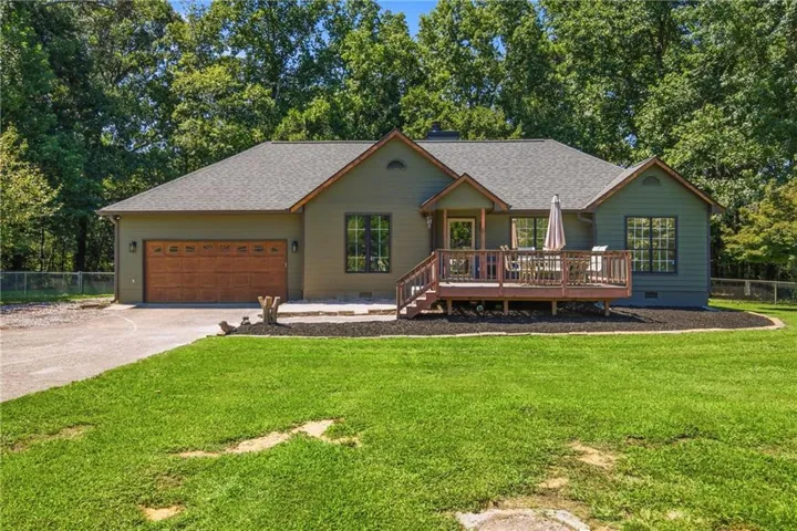 Ranch-style residence featuring a dark green exterior, wood-finish garage door, prominent front deck, and a shingle roof