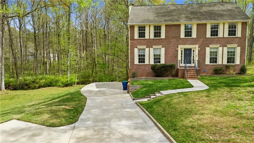 Colonial home with roof with shingles, brick siding, and a front lawn