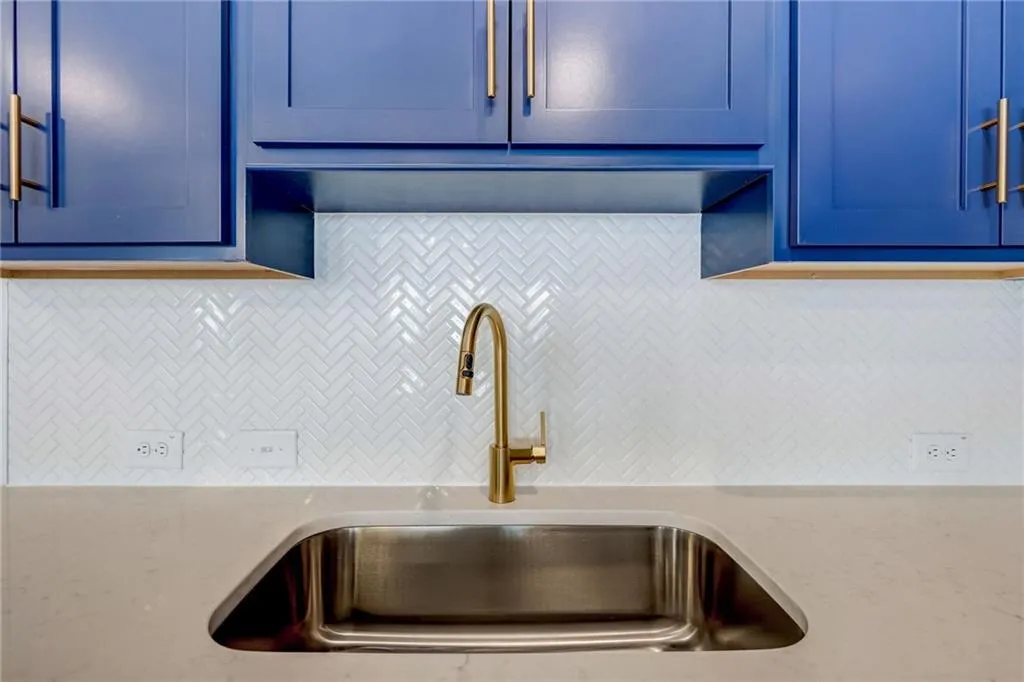 Kitchen featuring blue cabinets, decorative backsplash, and light stone counters