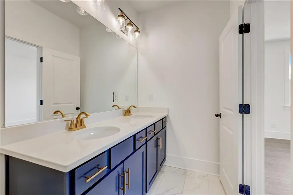 Full bath featuring double vanity and marble look tile flooring