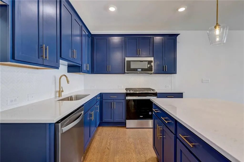 Kitchen with blue cabinetry, stainless steel appliances, light wood finished floors, backsplash, and recessed lighting