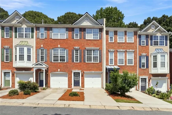 Brick townhome exterior featuring multiple bay windows, individual garages, and covered entryways