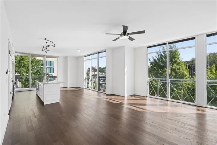 Expansive living area with wood-finish flooring, floor-to-ceiling windows, and a central kitchen island with a light-toned countertop