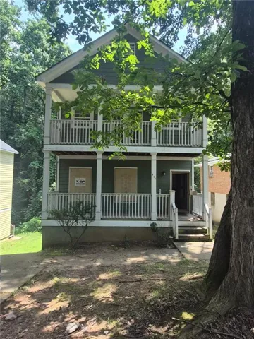 Two-story exterior with two balconies featuring white railings, and mature trees providing natural shading