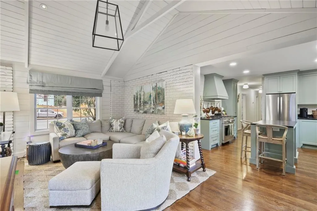 Living room featuring high vaulted ceiling, brick wall, and wood finished floors