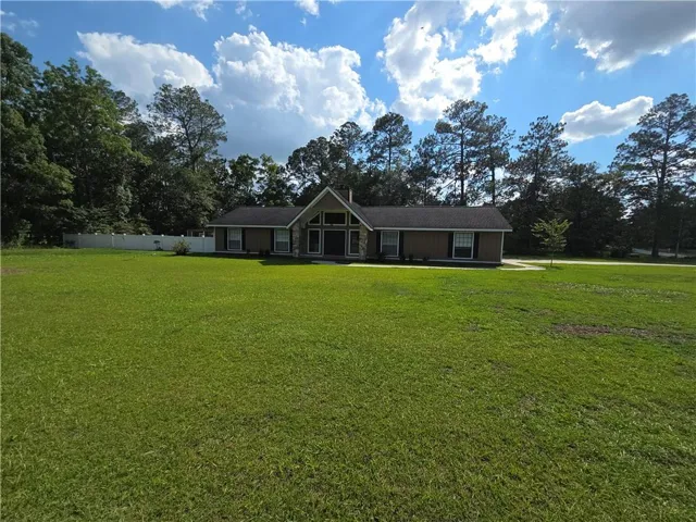Ranch-style residence featuring a prominent front lawn, gabled roofline, and stone column accents