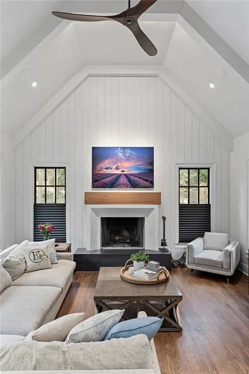 Living area with vaulted ceiling, hardwood / wood-style flooring, a fireplace with raised hearth, healthy amount of natural light, and ceiling fan