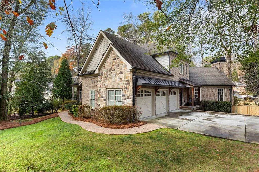 View of property exterior featuring stone siding, concrete driveway, roof with shingles, and a chimney