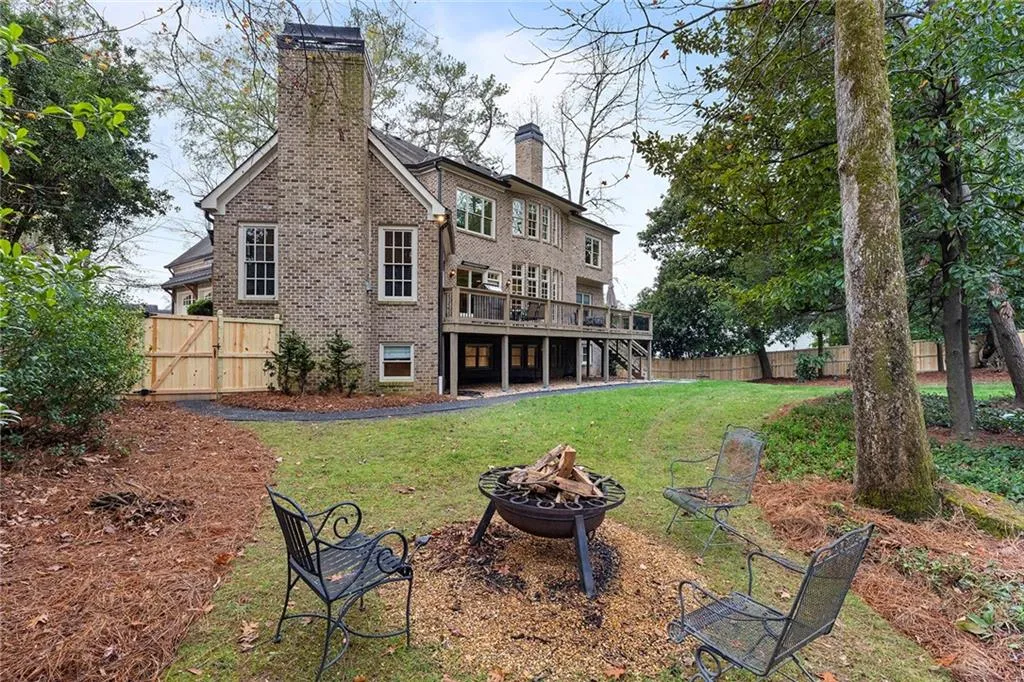 Rear view of house featuring a chimney, brick siding, a wooden deck, a fenced backyard, and a fire pit