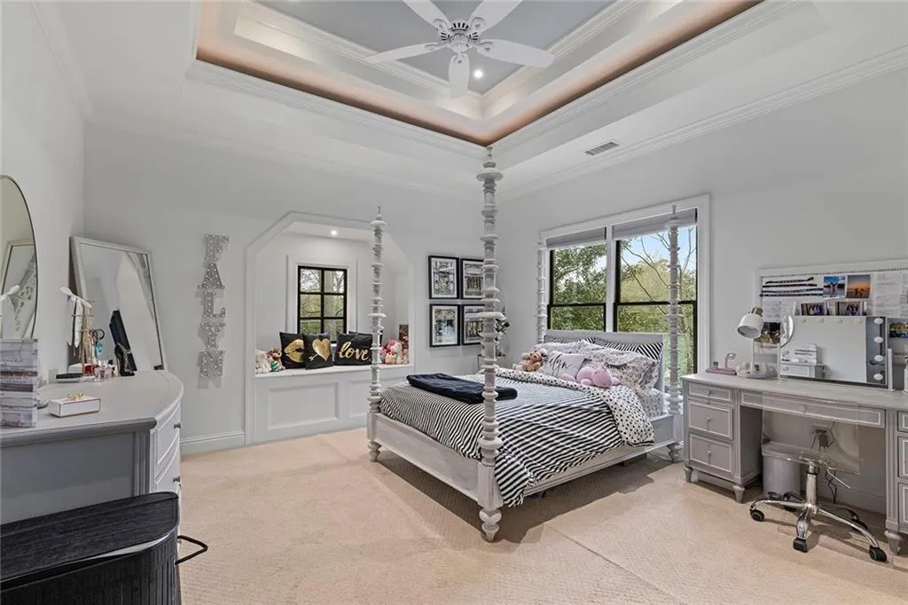 Bedroom with a tray ceiling, light carpet, ornamental molding, a ceiling fan, and a desk