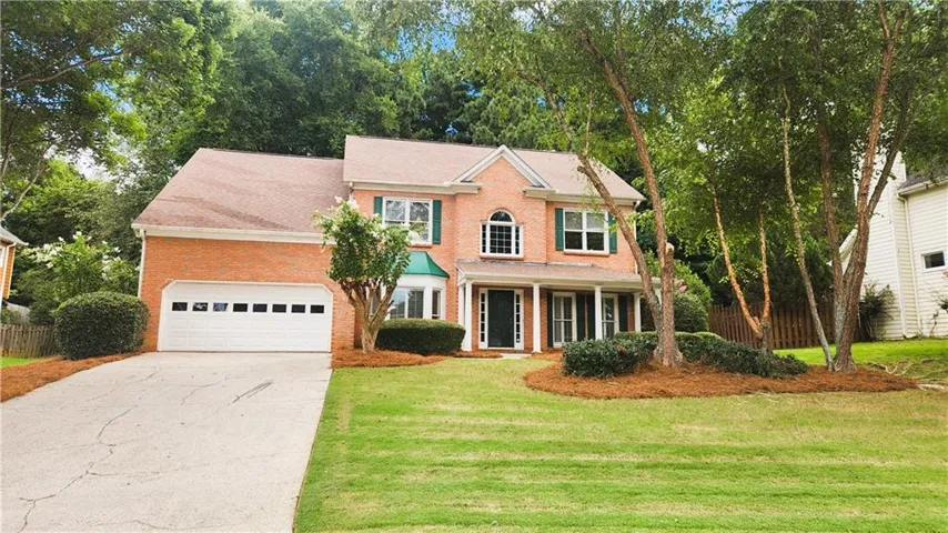 Colonial house with brick siding, concrete driveway, covered porch, and a garage