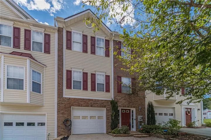 Three-story townhome featuring brick and siding facade, bay window, red shutters, and an integrated garage