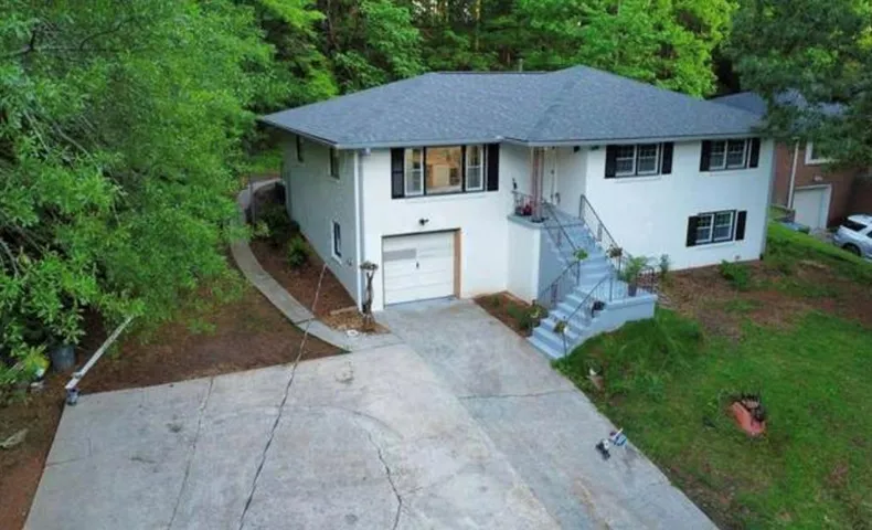 White exterior with contrasting black window shutters, a gray shingle roof, and a single-car garage