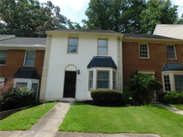 Two-story townhouse with white stucco facade, a dark entry door with an arched surround, and a bay window on the main level