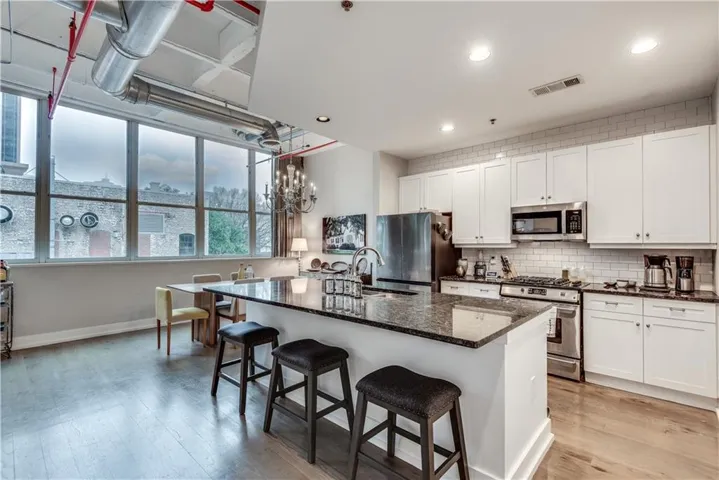 Open-concept kitchen with white shaker cabinetry, stainless steel appliances, and a dark stone countertop island
