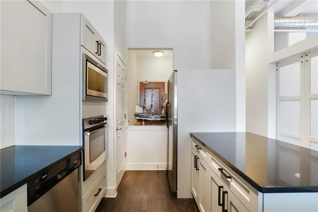 Kitchen with dark wood-style floors, appliances with stainless steel finishes, dark stone counters, and white cabinets