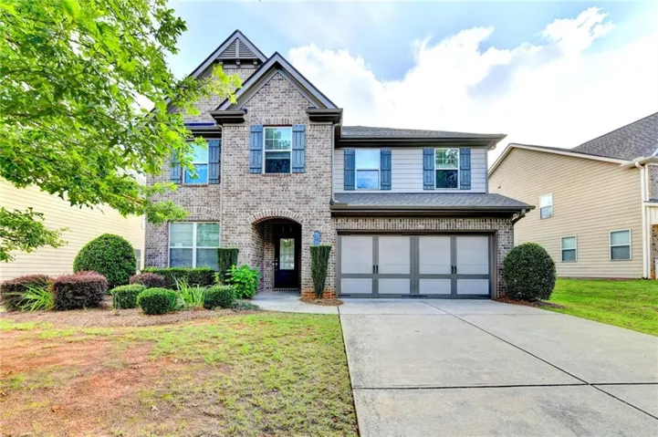 Two-story home featuring a brick and siding exterior, arched entryway, and a two-car garage with decorative paneling