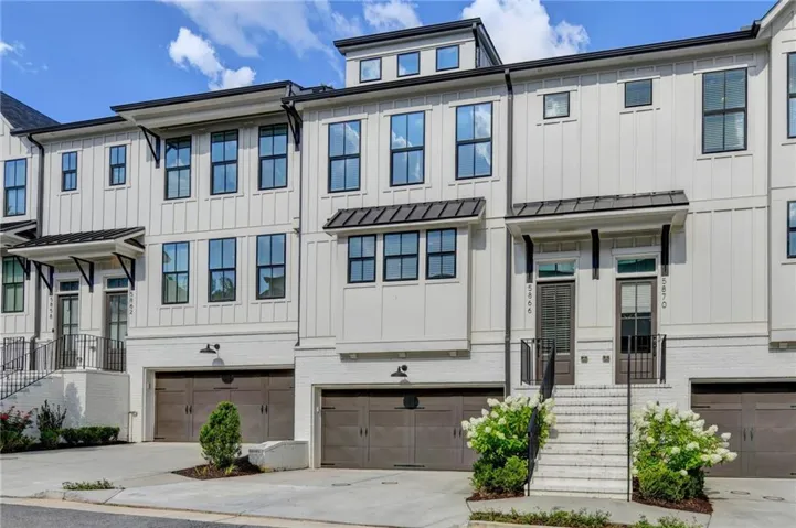 Modern farmhouse-style townhome featuring vertical white siding, black-framed windows, and a black metal roof over the front entrance