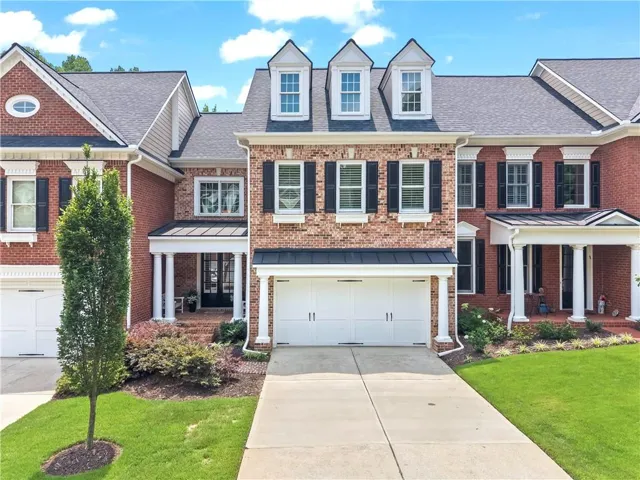 Brick exterior with dormer windows, a two-car garage, covered entry, and manicured landscaping