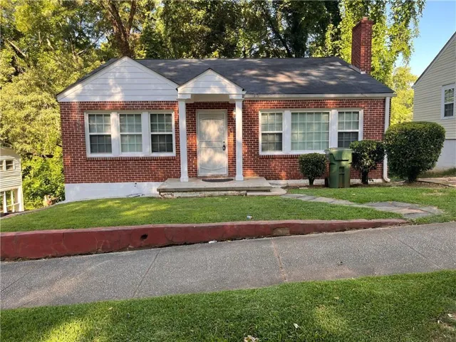 Brick exterior home featuring white trim, a covered front entry, and a prominent brick chimney