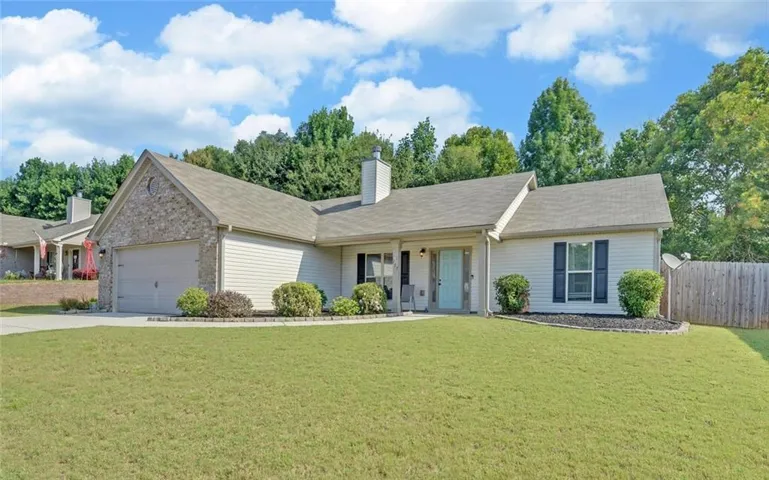 Charming single-story home featuring a brick and vinyl exterior, covered front porch with columns, and a spacious manicured lawn bordered by mature landscaping