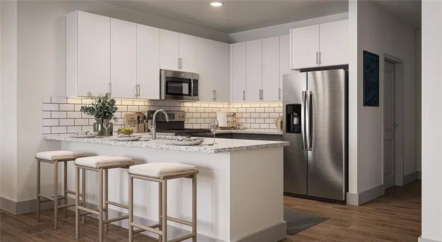 Modern kitchen featuring a breakfast bar with seating, white shaker-style cabinetry, stainless steel appliances, speckled countertops, and wood-finish flooring