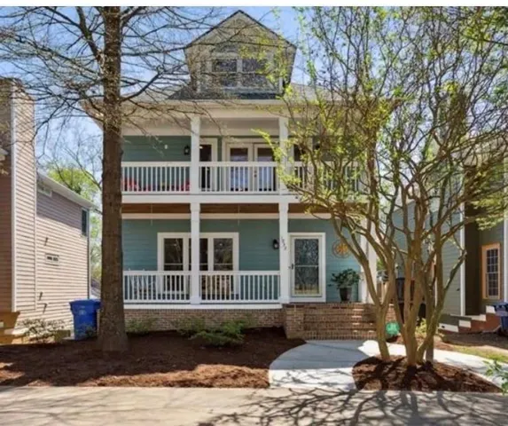 Two-story residence featuring a third-story dormer, dual-level covered porches with white railings, a brick foundation, and a concrete walkway
