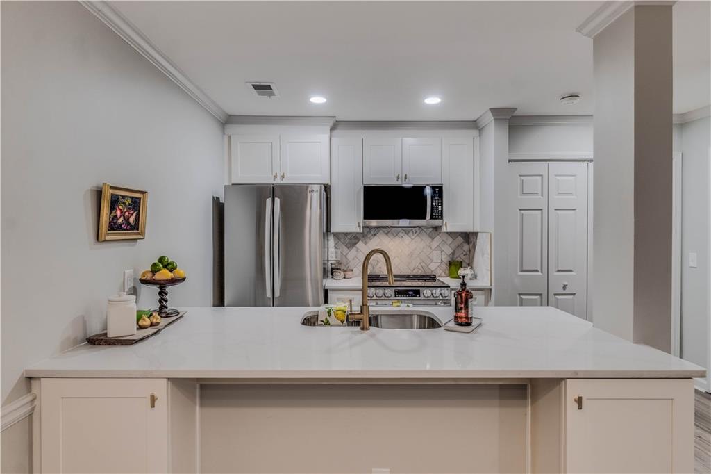 Kitchen featuring ornamental molding, tasteful backsplash, white cabinetry, and stainless steel appliances