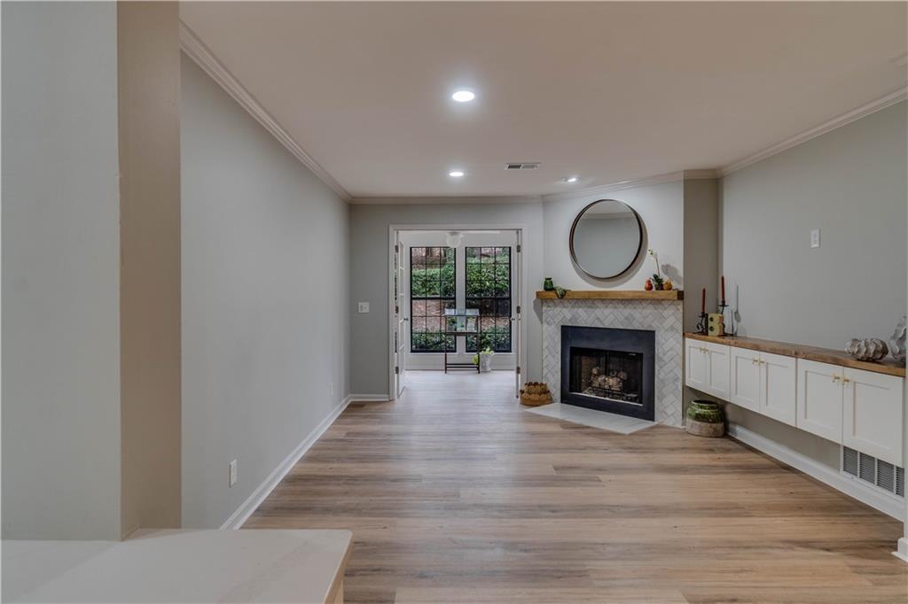 Living room featuring crown molding, a tiled fireplace, light wood-type flooring, and french doors