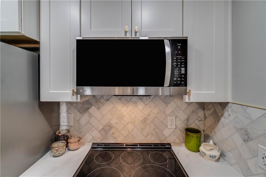 Kitchen featuring cooktop, white cabinetry, light stone counters, and backsplash
