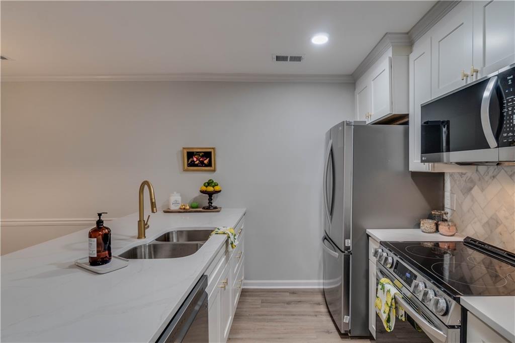Kitchen featuring light stone countertops, white cabinets, stainless steel appliances, sink, and light wood-type flooring
