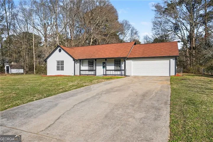 White exterior siding with dark trim, red shingle roof, attached garage, concrete driveway, and a front porch with dark railing